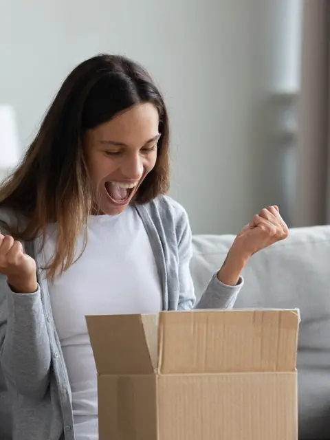 Eine Frau auf dem Sofa freut sich über ein gerade geöffnetes Paket